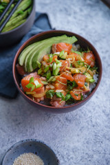 Poke bowl with raw marinated salmon, cucumbers and avocado. Top view on textured background