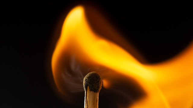 Burning wooden match with a red match head on a black background.