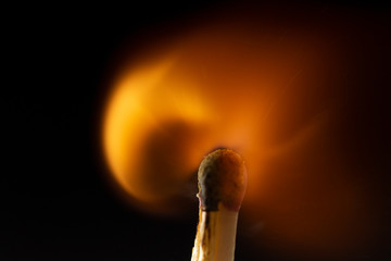 Burning wooden match with a red match head on a black background.