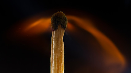 Burning wooden match with a red match head on a black background.