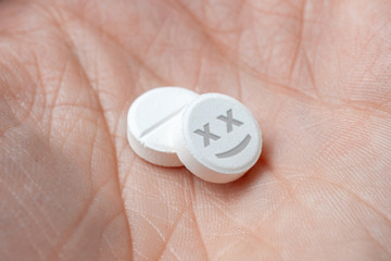 Two white pills with dead face drugs in hand. closeup