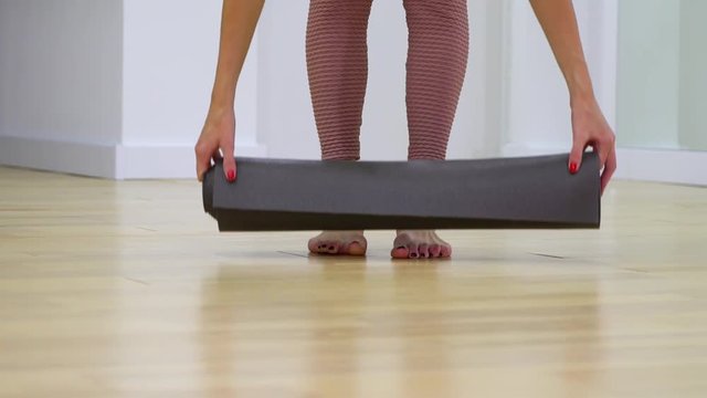 view of young woman feet unrolling mat and sitting on it in slow motion. Sports, recreation, health concept