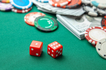 Concept of gambling in casino, sports poker. Red gaming dice and colored chips with cash cash dollars on green gaming table.