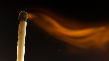 Burning wooden match with a red match head on a black background.