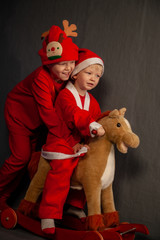 Happy children are dressed in festive costume of Santa Claus and snowman, carrying decorated Christmas tree with balls and garlands on yellow car, accompanied by rocking horse. Christmas Eve