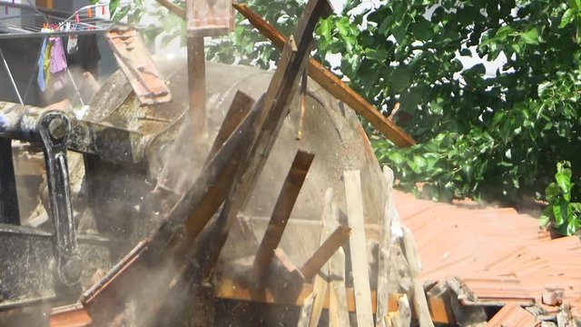 Slow motion Hydraulic arm pounding and crushing the roof. An excavator turns old home into rubble and dust fills the air. Falling down broken roof tiles and planks during demolition of a house. SM