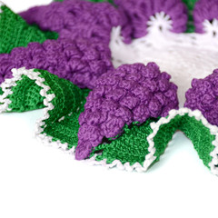 A part of isolated crocheted doily in shape of a violet grape with green leaves.