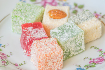 Traditional turkish delight on a plate on white wooden background. Assorted Oriental sweets.