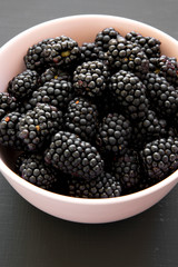 Blackberries in pink bowl on dark surface, low angle view. Summer berry. Close up.