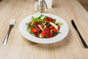 Carpaccio plates ready to serve on the table. Carpaccio in a white bowl on a wooden table. Middle plan.