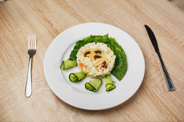 Beautifully tailored salad garnished with mushrooms and fresh cucumbers. Russian traditional salad olivier in white plate