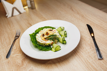 Beautifully tailored salad garnished with mushrooms and fresh cucumbers. Russian traditional salad olivier in white plate
