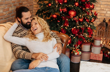 Christmas. Couple. Home. Togetherness. Man and woman are hugging and laughing near the Christmas tree