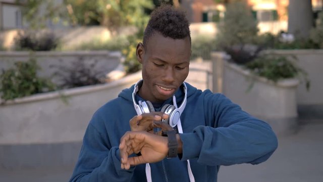 Modern young black african man using smart watch to listen music-outdoor
