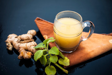 Close up of organic juice of ginger in a transparent glass on wooden surface with some raw ginger...