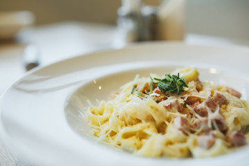 Pasta with chicken and tomatoes with lettuce leaves in a white plate. Close up