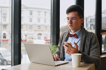 business man sitting at a table in a cafe with a smartphone using a laptop