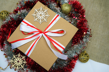 Fototapeta na wymiar The brown gift box is tied with white red ribbon, Christmas decorations, tinsel, snowflakes and Christmas balls