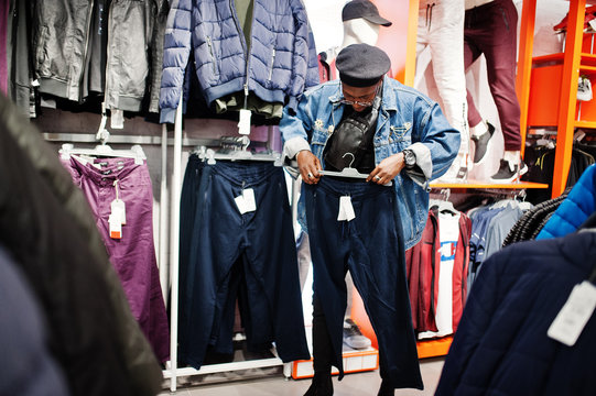 Stylish casual african american man at jeans jacket and black beret at clothes store looking on new sport pants.