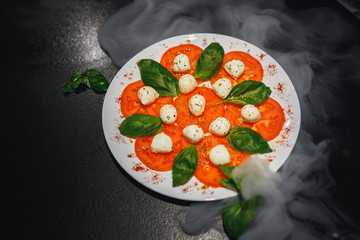 Tomatoes with mozzarella and rosemary on white plate isolated on black background. Close up