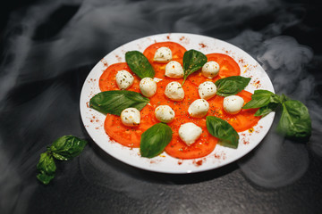 Tomatoes with mozzarella and rosemary on white plate isolated on black background. Close up