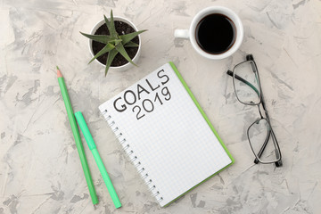 goals for 2019. text in notebook with glasses, coffee, and a flower on a light background.