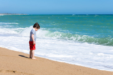 Fototapeta na wymiar A boy plays on a sandy beach at the water's edge