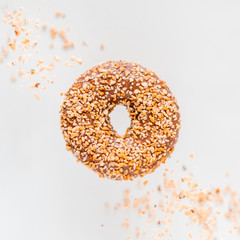 A donut covered with milk chocolate glaze and nut crumb levitates on a white background. Sweet food concept.