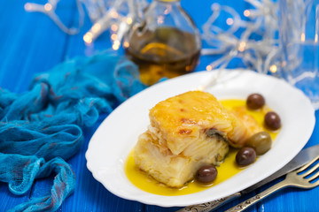 fried cod fish with olives and olive oil on white dish