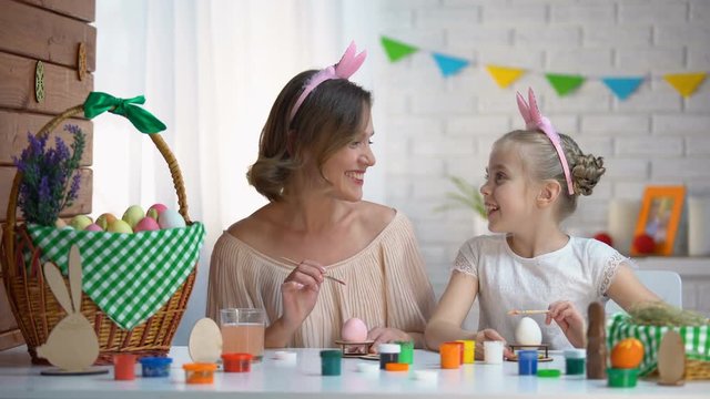 Little daughter kissing mother on cheek helping with Easter eggs decor, love