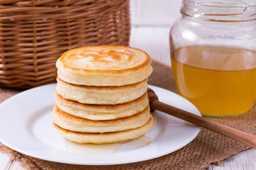Stack of pancakes with honey in plate on white table