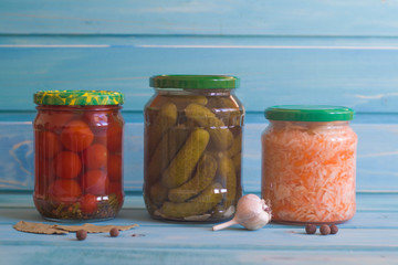 Gherkins, tomatoes and sauerkraut in jars on a blue wooden background.