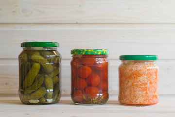 Gherkins, tomatoes and sauerkraut in jars on a light wooden background.