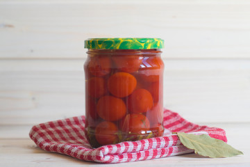 Salted red tomatoes in a jar on a red napkin on a light wooden background.