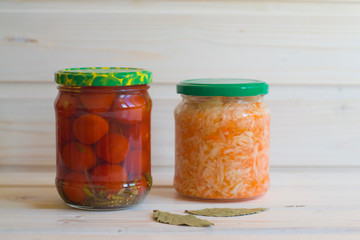 Salted tomatoes and sauerkraut in jars on a light wooden background.