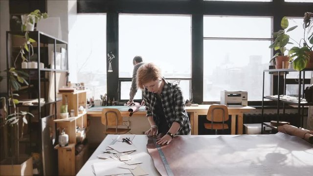 Young man and woman working in a light trendy manufacturing workshop with big piece of leather material on a table.