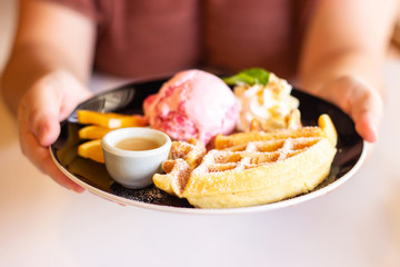 Woman hand holding plate of homemade waffle served with strawberry ice cream. Sweet dessert.