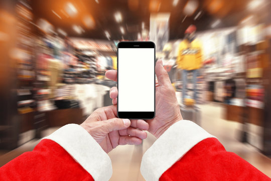 Santa Claus holding smartphone with isolated screen, clothing store in background. Christmas shopping concept