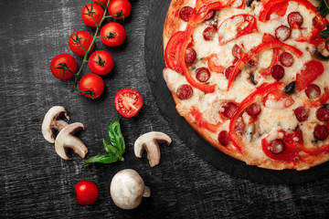 Pizza with smoked sausages, cheese, mushrooms, cherry tomatoes, bell peppers and greens on a stone.