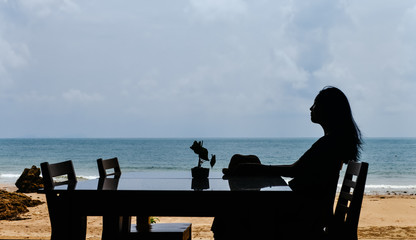 single Asian young woman sits at dining table by window at tropical beach, Lanta island, Krabi, Thailand.