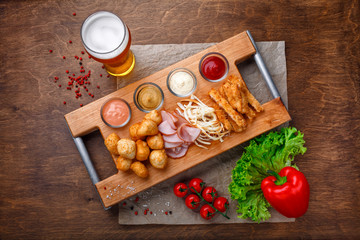 Big set of snacks for beer it includes fried cheese balls, pigtail cheese, ham and crab sticks on a wooden board