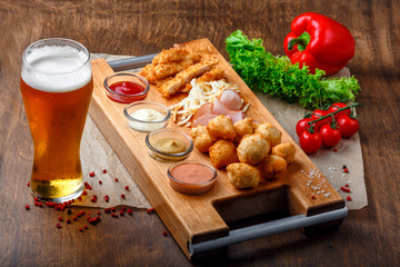 Big set of snacks for beer it includes fried cheese balls, pigtail cheese, ham and crab sticks on a wooden board