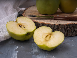 Two green golden apples cut in two halves on a wooden platter. In the background are whole apples.