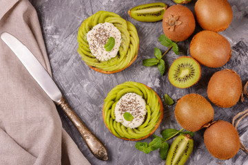 Delicious healthy tartlets filled with cheese cream and topped with kiwi slices in swirl and chia seeds. Healthy dessert concept.