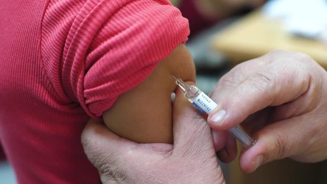 Doctor makes vaccination in the children's hands. Injection of a syringe in the shoulder close-up. 4k