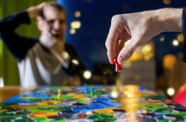 Your move - board game concept. Hand holding game figure in the air - making move and man watched the game and shock from the action move. Board game field, many figures dark blurred background