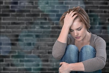 Worried woman sitting holding knees with arm on background