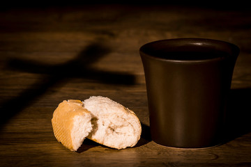 The concept of the multiplication of bread and wine in the Christian religion, bread and a cup of wine against the shadow of the cross