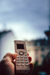 man hand holding outdoor home office white cordless phone dialing a number on the white keyboard shallow depth of field and gray clouds in background