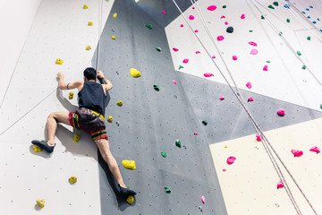 Rear view of man climbing wall with help of grip - obrazy, fototapety, plakaty